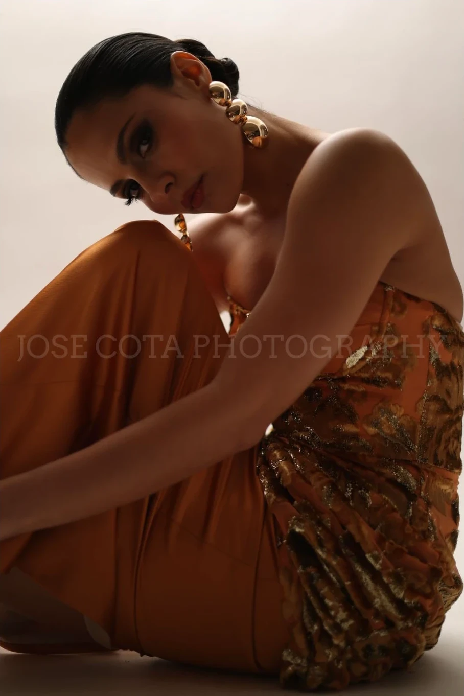 Modelo sentada con The Lumiére Dress, brocado dorado y satín cobre